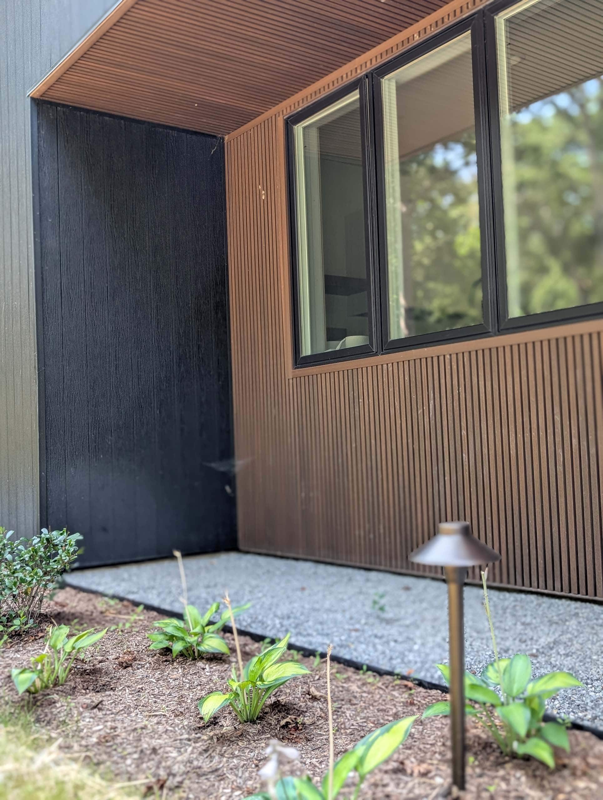 Residential window with 3 transparent glass panes with black trim, seen from the outside with thin vertical wood panels on the exterior walls