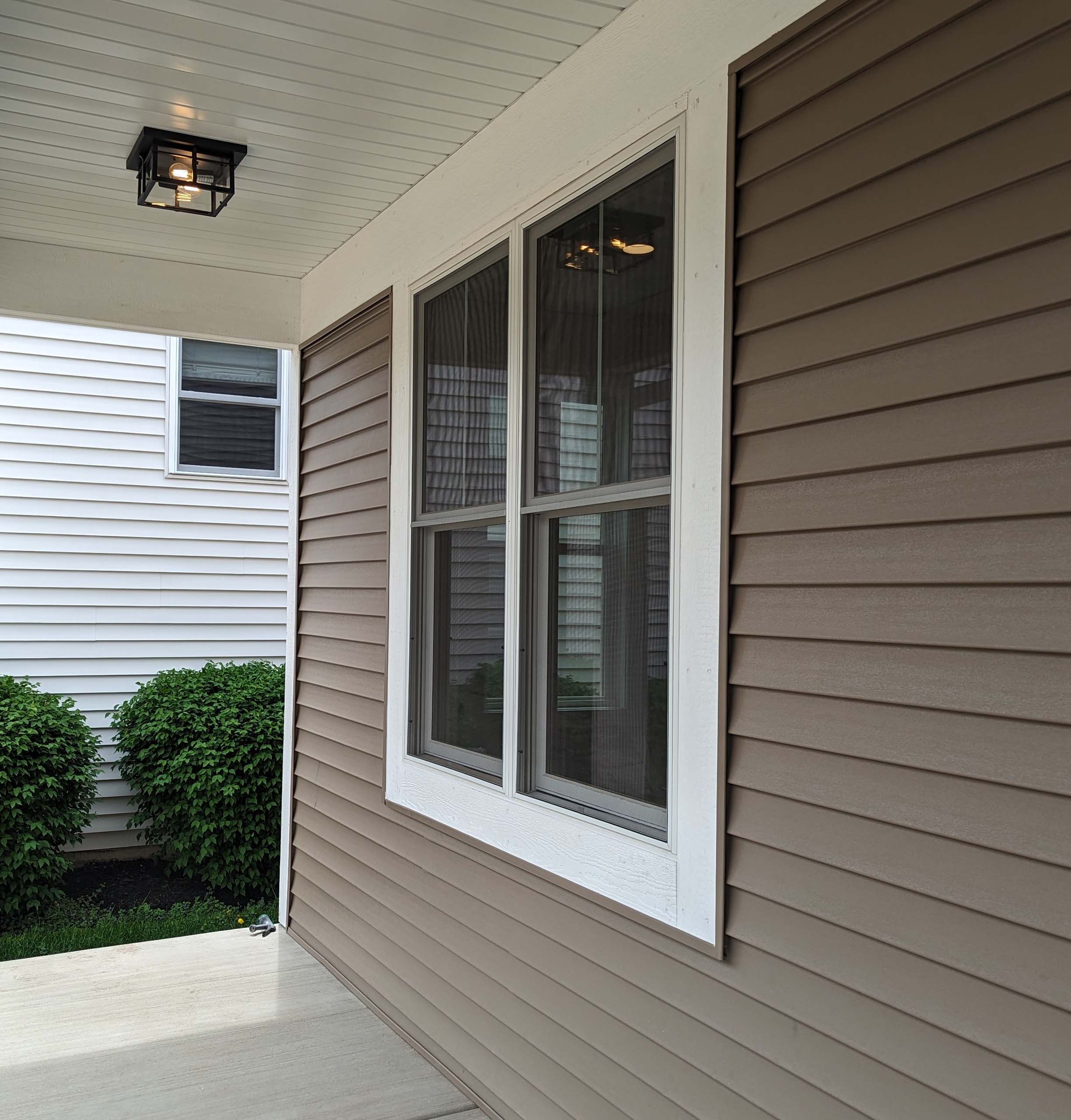 Residential window with 4 transparent glass panes and white trim seen from the outside porch with grey siding